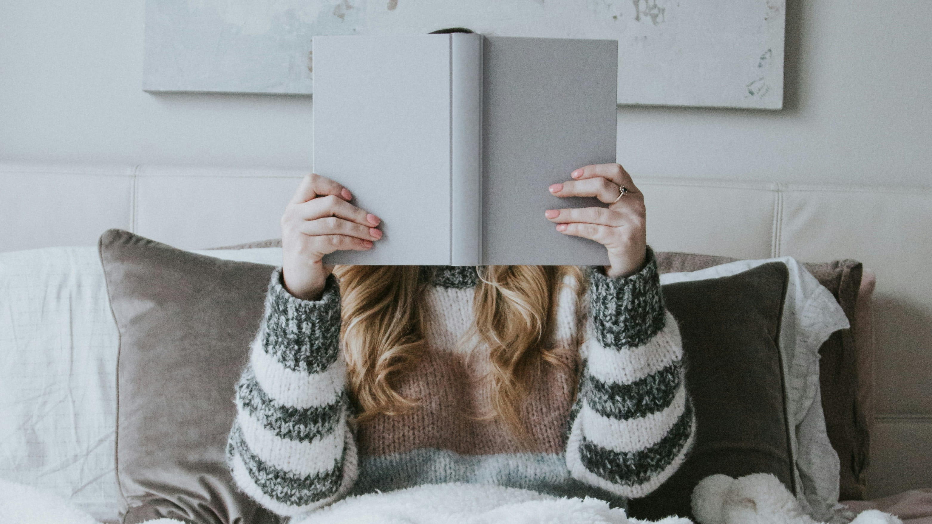 Girl reading book that covers her face, wearing cosy winter clothes.