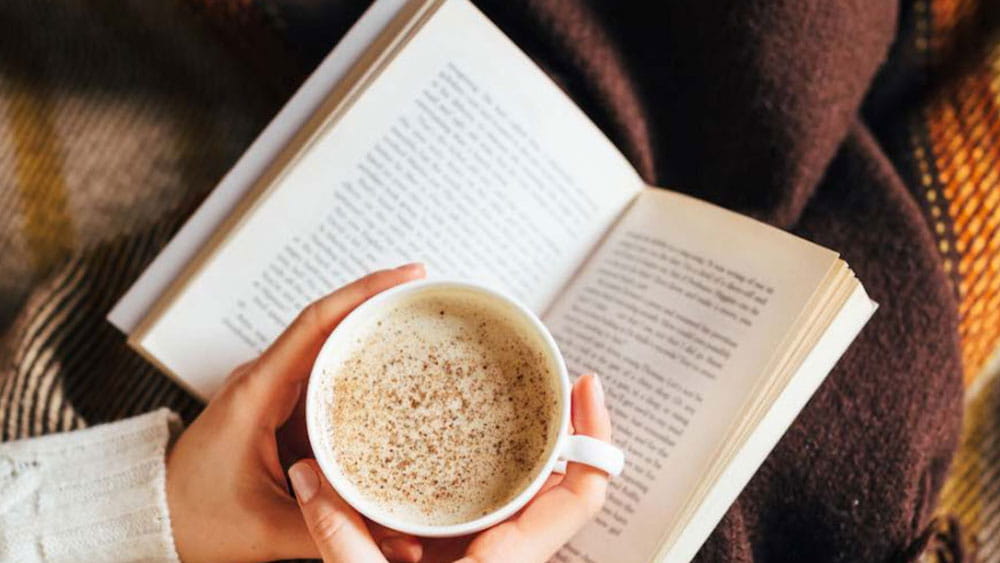 person reading book while drinking coffee