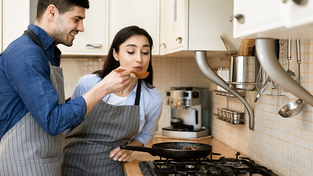 Couple tasting food from simmering pan on gas cooktop